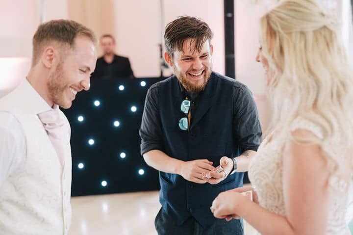 Greg Holroyd performing close-up magic at a UK wedding—bride and groom react with laughter and surprise during card trick